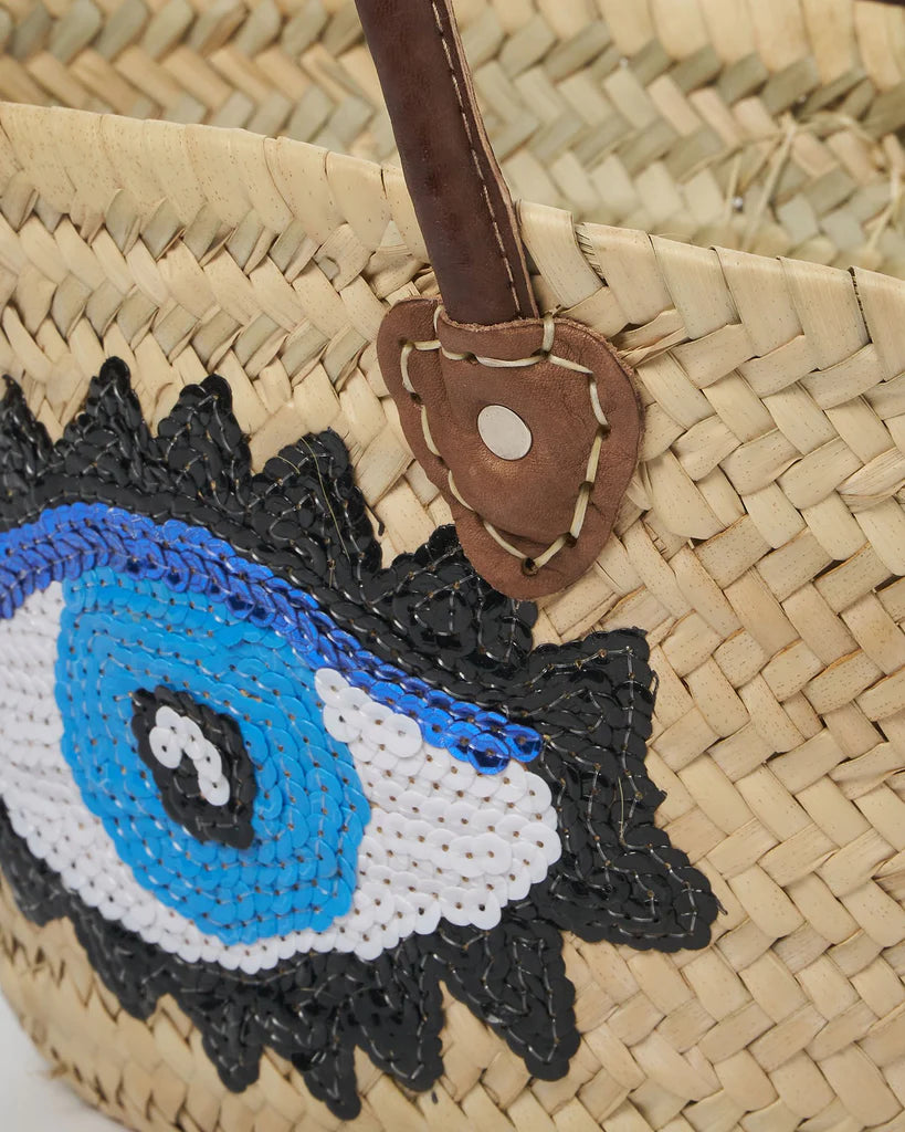 Handwoven Moroccan straw beach bag featuring a blue evil eye design with genuine leather handles.