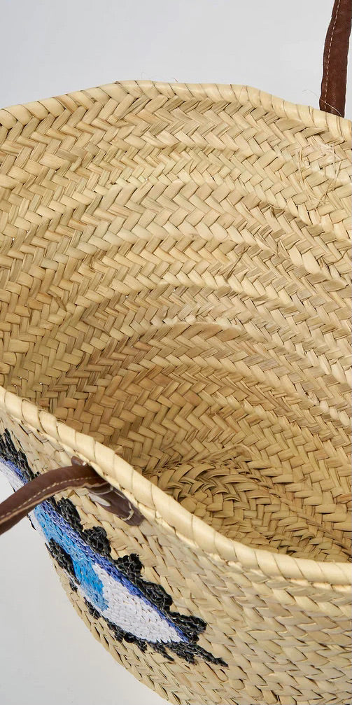 Handwoven Moroccan straw beach bag featuring a blue evil eye design with genuine leather handles.