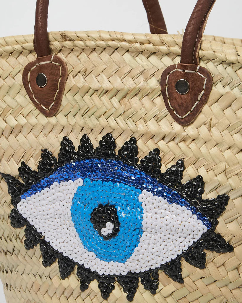 Handwoven Moroccan straw beach bag featuring a blue evil eye design with genuine leather handles.
